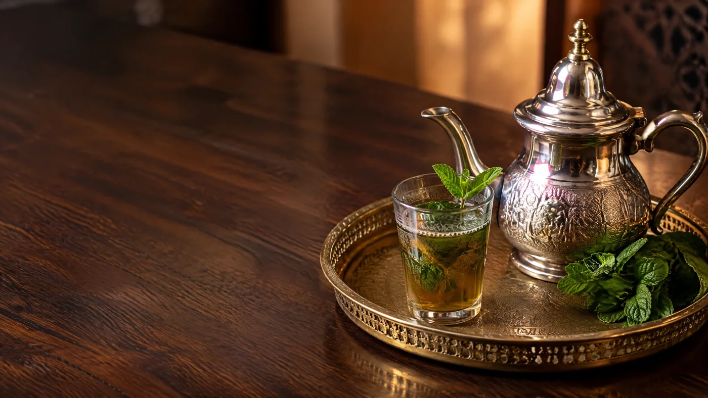 Moroccan mint tea served in a glass beside a silver teapot